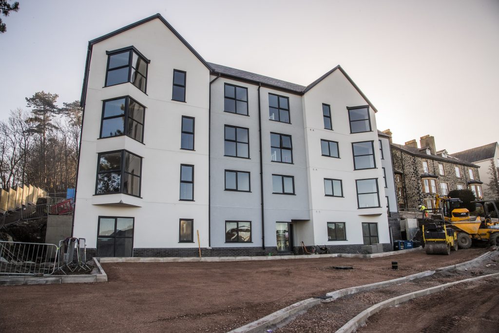 Modern white apartment block with black window frames, blue sky and large tree