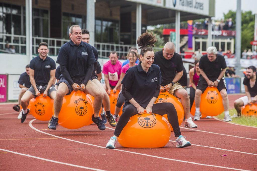 Group of staff members bounce on orange space hoppers on a race track