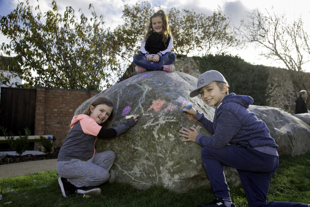 three of our young tenants smile and draw with colour chalk on our Tre Cwm rock caterpillar