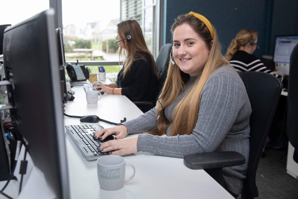 Female staff member smiles with a headset as she types on her keyboard