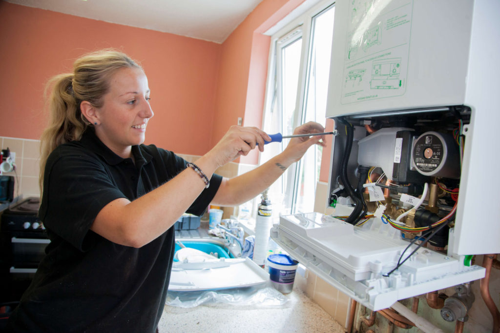 A female plumber smiles as she uses a tool to fix a boiler